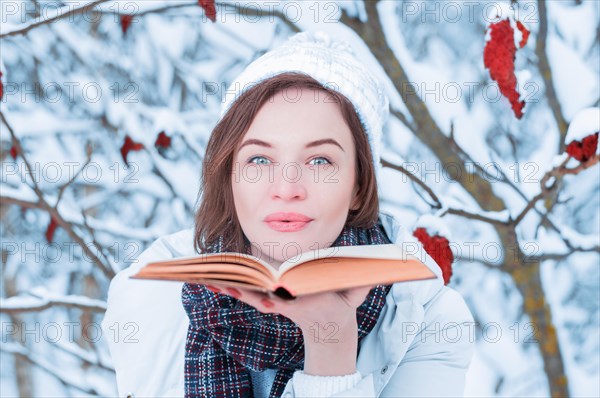 Beautiful girl blowing on the pages of the book. Snow is falling in the winter forest. Christmas concept.