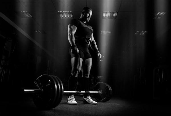 The weightlifter is preparing to perform an exercise called deadlift. He stands directly above the barbell and looks at it