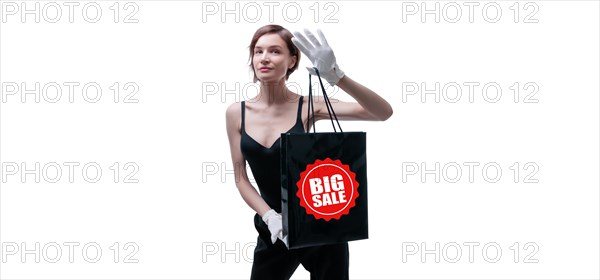 Beautiful young woman in white gloves holds a black craft bag in her hand. Shopaholics concept. Spenting. Gifts for the holidays. Black Friday. Shopping centers