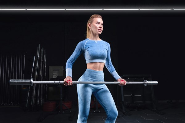 Athletic physique woman posing with a barbell in her hands. The concept of sports
