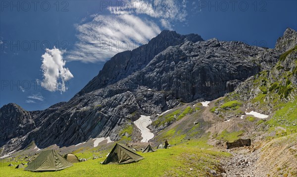 Tents of mountain hunters in the foreground with imposing mountain cliffs and blue sky with foehn clouds in the background