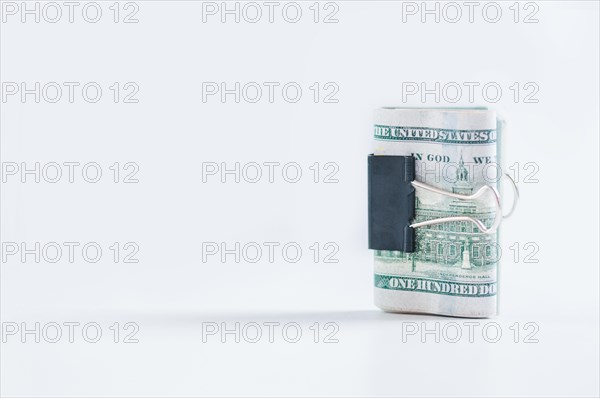 Pack of hundred-dollar bills lies on a white table fastened with a paperclip. The concept of savings during the crisis.