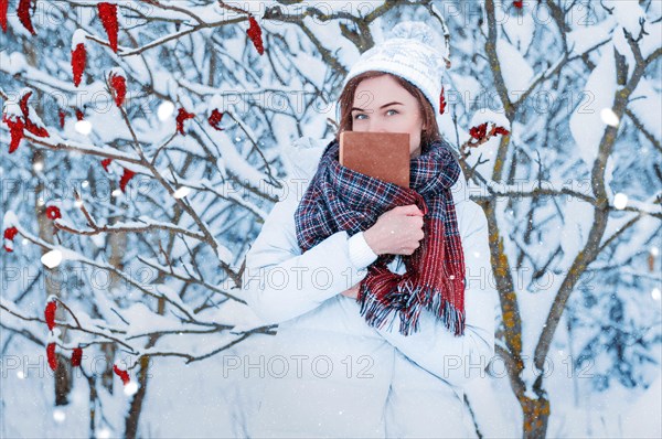 The girl walks through the winter forest. She covered her face with a book. Learning concept. Winter's tale.