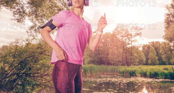 Portrait of a beautiful girl running in a sunny park in headphones with a smartphone. Music apps concept.