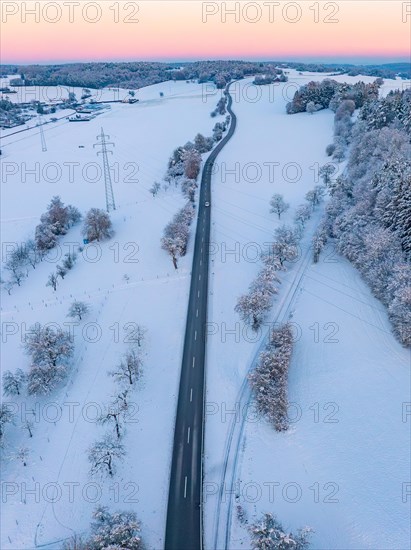 An empty road runs through a wintry landscape in the twilight