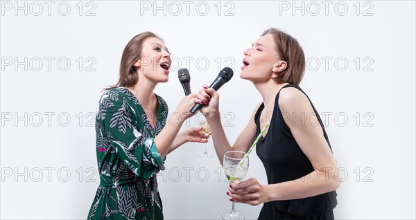 Portrait of two singing girls with glasses in their hands. Karaoke concept.