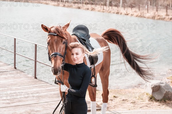 Beautiful stylish woman walking with a horse in a country club. Equestrian sport