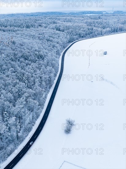 A winding road runs through a wintry landscape with snow-covered fields