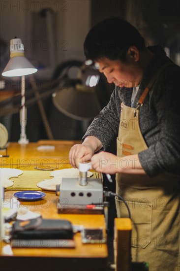 Asian Master luthier lute maker artisan both hands performing bend controller purfling strips process in iron tool for a new raw back and front plates of classic handmade violin in his workshop in Cremona