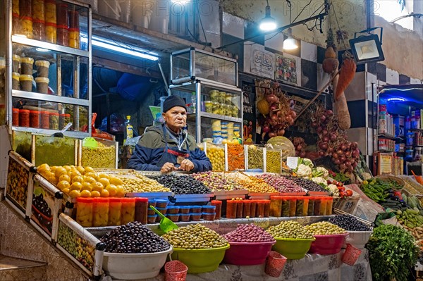 Moroccan vendor selling table olives at food market in the city Meknes