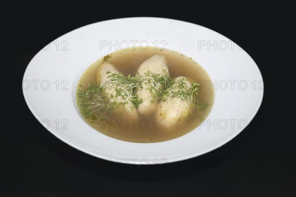 Three semolina dumplings swimming in a beef broth in a white porcelain plate