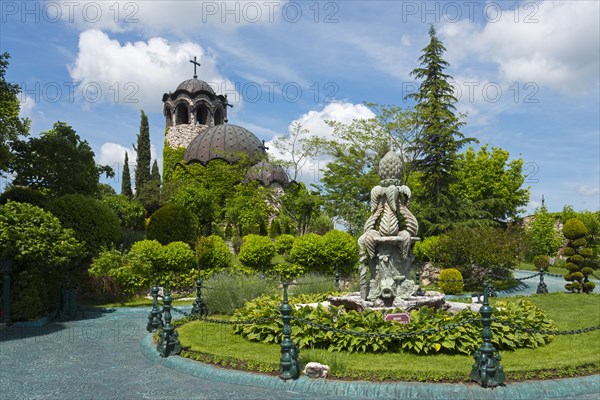 Church with dome next to a well-tended garden with sculpture and blue waterway