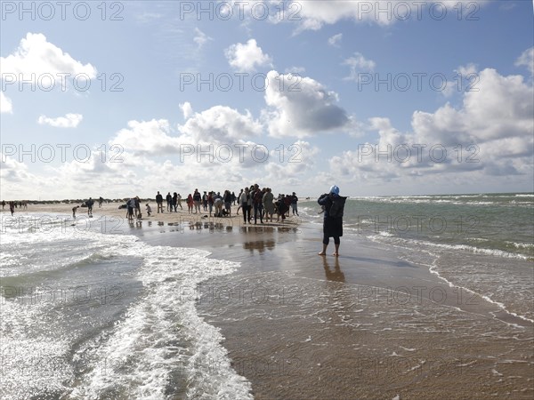 Tourists stand with one foot in the North Sea and one in the Baltic Sea in Grenen or Skagens Gren