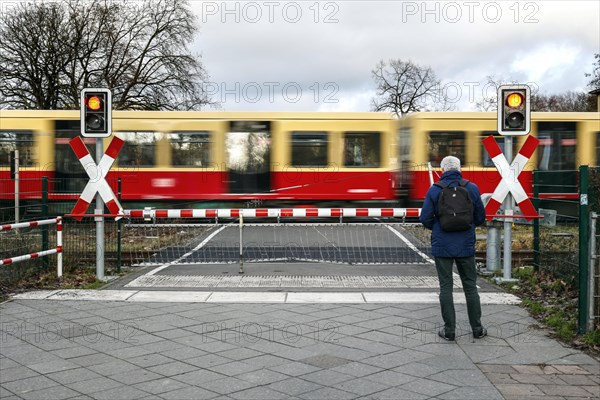 A man waits at a level crossing with a barrier while an S-Bahn train passes through