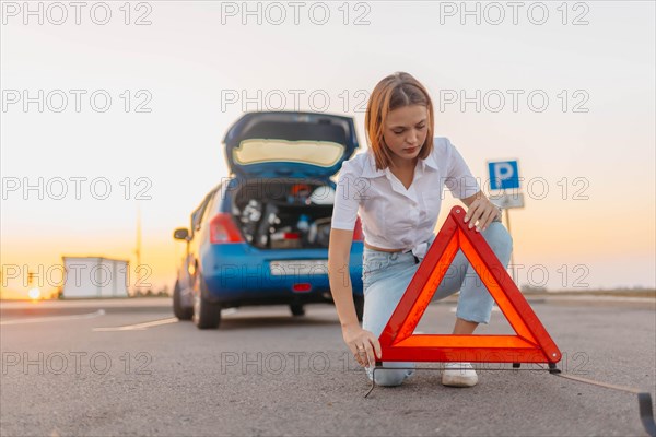 Young beautiful and hot woman driver installs a warning triangle