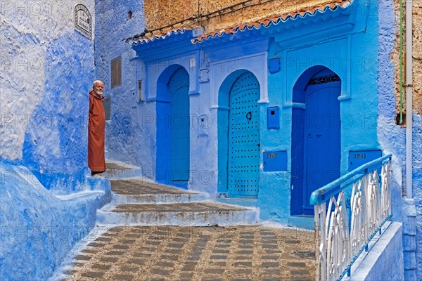 Muslim man wearing traditional djellaba in alleyway with blue houses and doors in medina