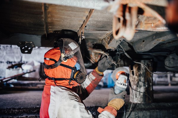 Male car service worker cleans the bottom of the car body with a grinder. Waterproofing metal of a car body