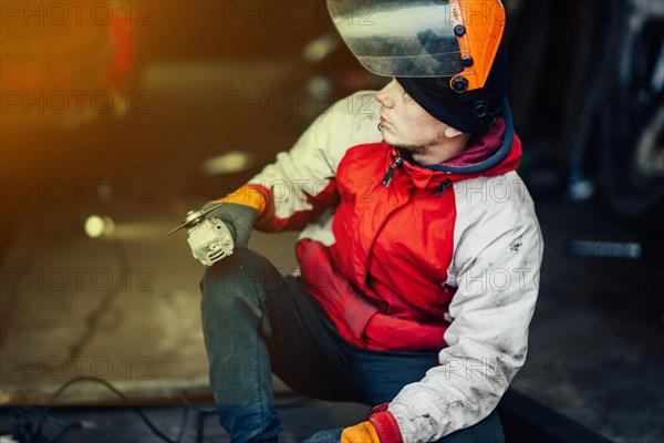 Man worker in a uniform and a mask works with a grinder