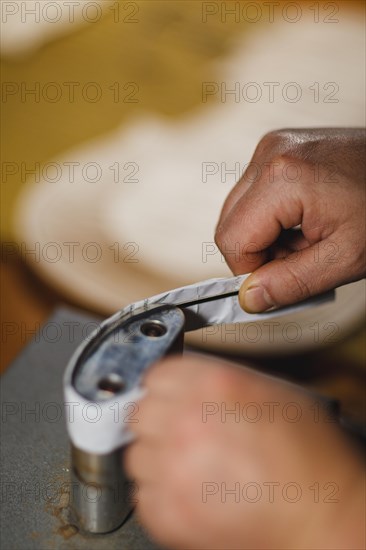 Unrecognizable luthier lute maker artisan both hands performing bend controller purfling strips process in iron tool for a new raw back and front plates of classic handmade violin in his workshop in Cremona