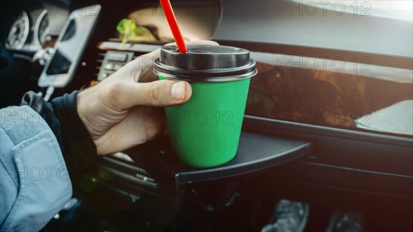 Cardboard cup of coffee inside a car in a passenger's hand