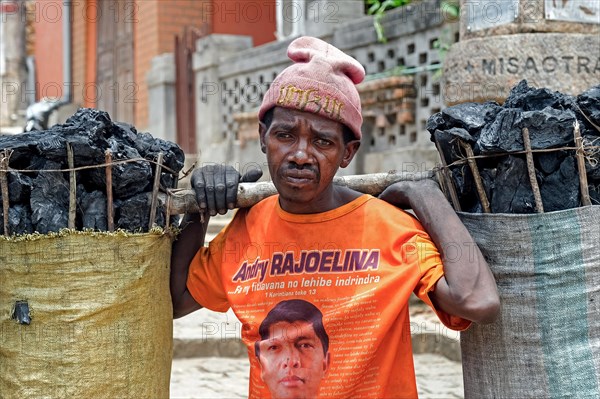 Malagasy man carrying big bags of charcoal on his shoulders in the city Fianarantsoa