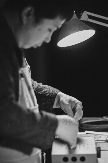 Asian master luthier lute maker artisan both hands performing bend controller purfling strips process in iron tool for a new raw back and front plates of classic handmade violin in his workshop in Cremona