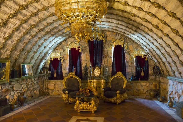 An opulently decorated room with throne chairs under a vaulted stone ceiling and a large chandelier