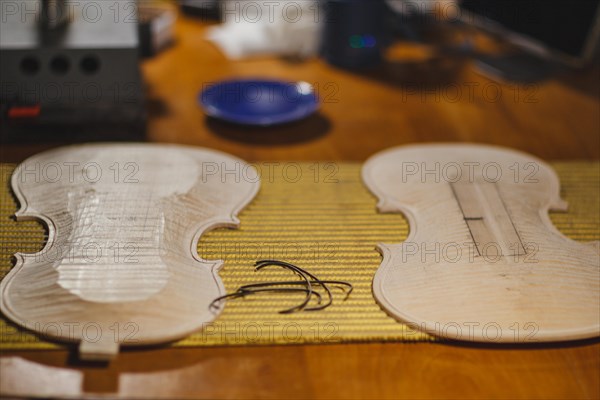 Front and back plates of new raw handmade classic violin on a workbench in violinmaker artisan workshop and purfling fillet made of evony and ivory or pear wood ready to be inserted in the carved all around the shape for aesthetic touch and prevent cracking