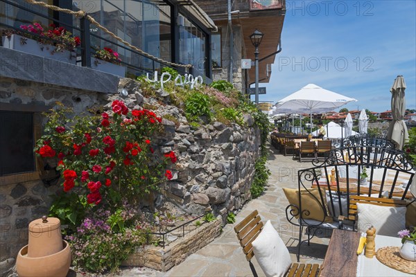 Inviting restaurant with terrace and blooming roses on a stone wall under a blue sky