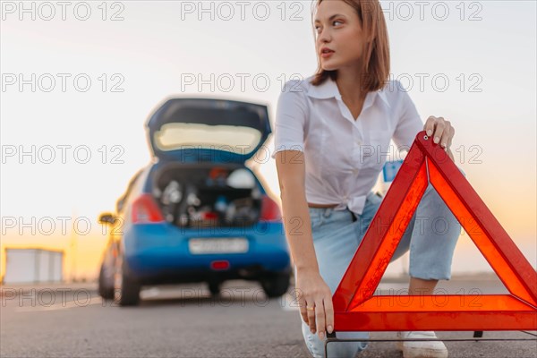 Young beautiful and hot woman driver installs a warning triangle