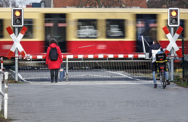 Two woman waiting at a level crossing with a barrier while an S-Bahn train passes through