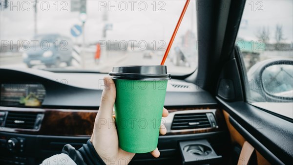 Cardboard cup of coffee inside a car in a passenger's hand