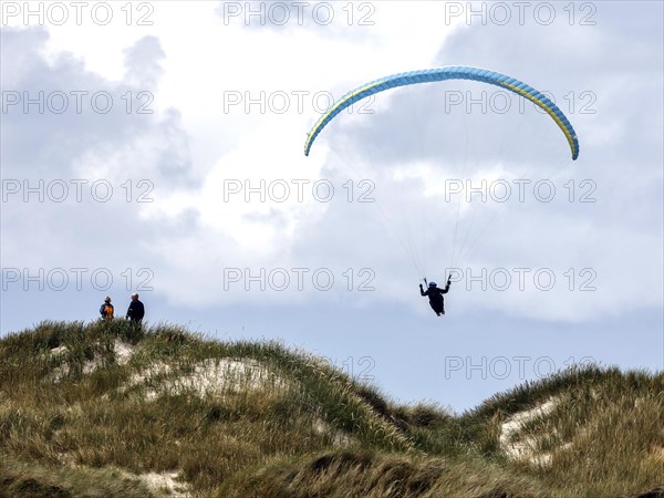 Paraglider flying over dunes on a beach in Vejers