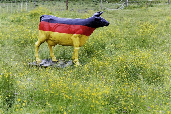 A life-size cow made of plastic in a flowering meadow