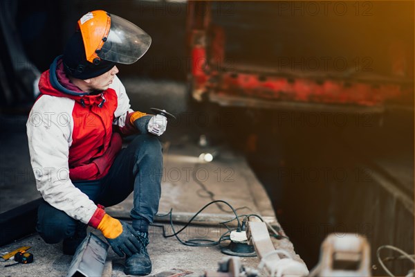 Man worker in a uniform and a mask works with a grinder