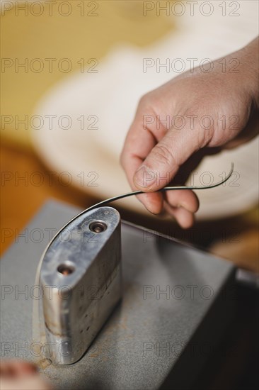 Unrecognizable luthier lute maker artisan both hands performing bend controller purfling strips process in iron tool for a new raw back and front plates of classic handmade violin in his workshop in Cremona