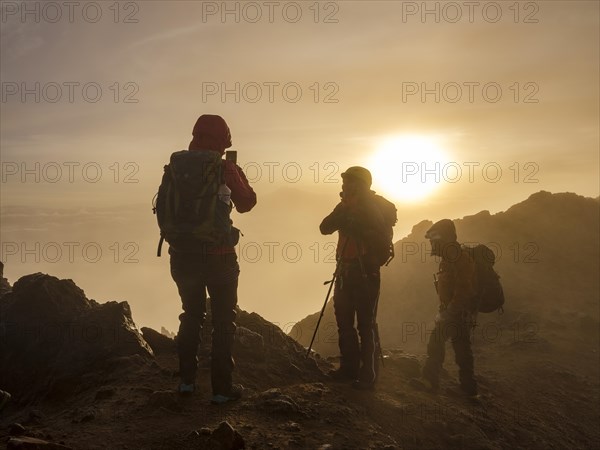Mountaineer taking photos with his mobile phone in the fog at sunrise