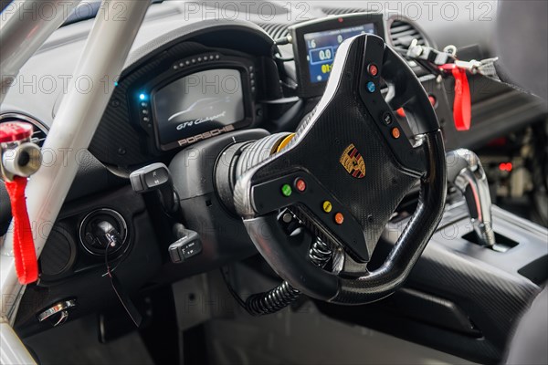 View into cockpit with digital display digital display modern steering wheel sports steering wheel of racing car racing version of Porsche Cayman GT4 Clubsport with in the centre logo coat of arms of car brand sports car brand manufacturer of sports car Porsche
