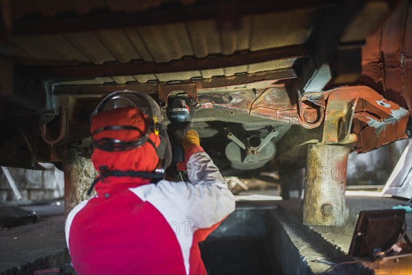 Male car service worker cleans the bottom of the car body with a grinder. Waterproofing metal of a car body