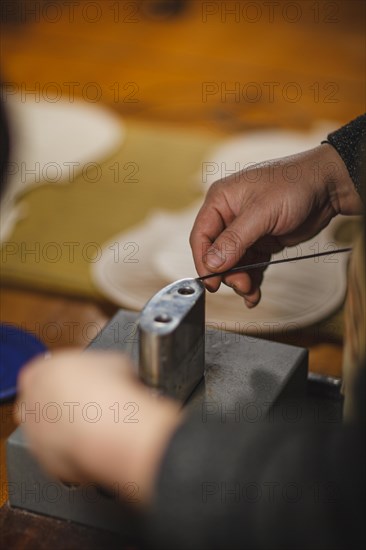 Unrecognizable luthier lute maker artisan hands in his workshop performing bend controller purfling strips process in iron tool for a new raw back and front plates of classic handmade violin in Cremona