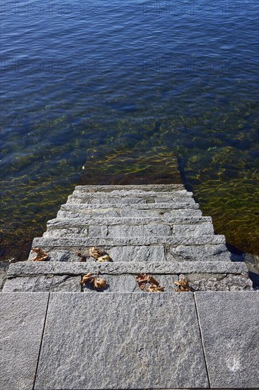 Steps into the water with dried leaves on the shore of Lake Maggiore in Ascona