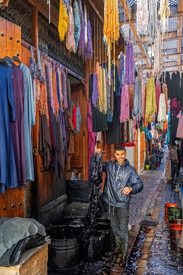 Moroccan man dyeing yarns and fabrics in alley of medina in the city Fes