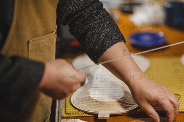 Unrecognizable luthier lute maker artisan both hands performing bend controller purfling strips process in iron tool for a new raw back and front plates of classic handmade violin in his workshop in Cremona