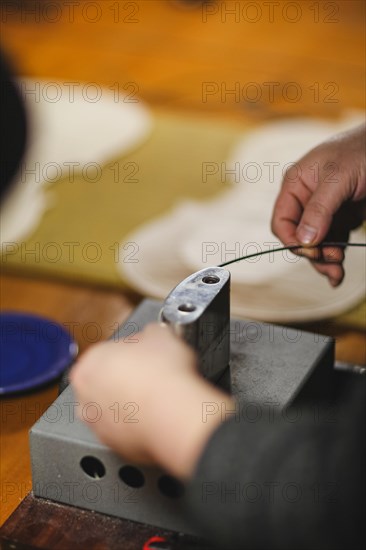 Unrecognizable luthier lute maker artisan hands in his workshop performing bend controller purfling process in iron tool for a new raw back and front plates of classic handmade violin in Cremona