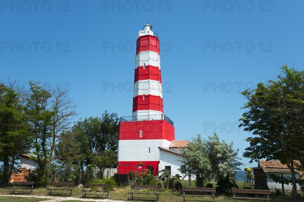 Red and white striped lighthouse surrounded by trees and a meadow under a blue sky