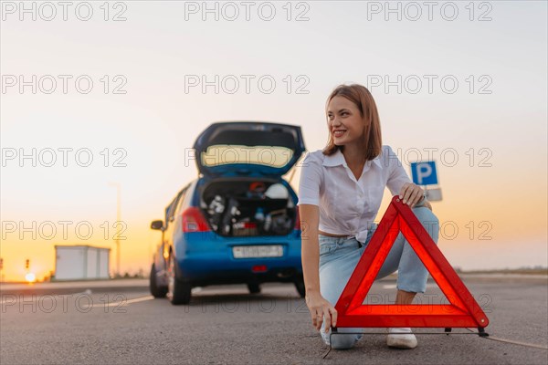 Young beautiful and hot woman driver installs a warning triangle