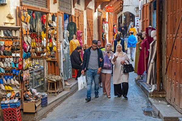 Moroccans walking in shopping street past shoe store and clothes shop in medina in the city Fes