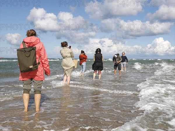 Tourists stand with one foot in the North Sea and one in the Baltic Sea in Grenen or Skagens Gren