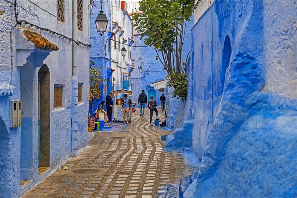 Moroccans in narrow alleyway with blue houses in medina
