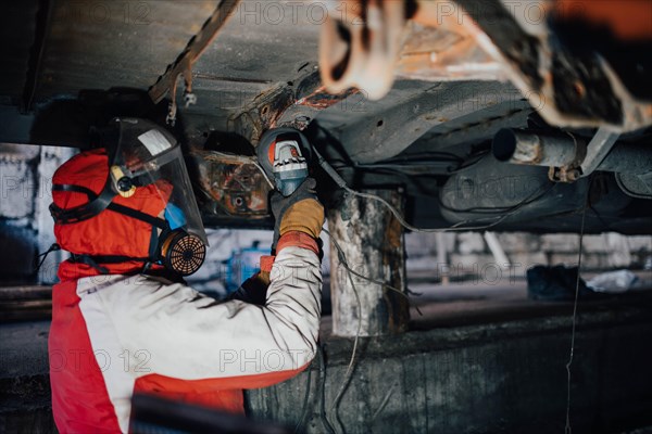 Male car service worker cleans the bottom of the car body with a grinder. Waterproofing metal of a car body